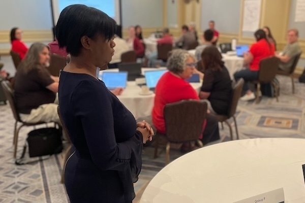 Veronica Womack stands next to a table and listens as an NDITA participant makes a comment during her interactive keynote session.