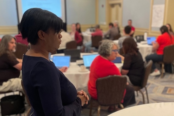 Veronica Womack stands next to a table and listens as an NDITA participant makes a comment during her interactive keynote session.