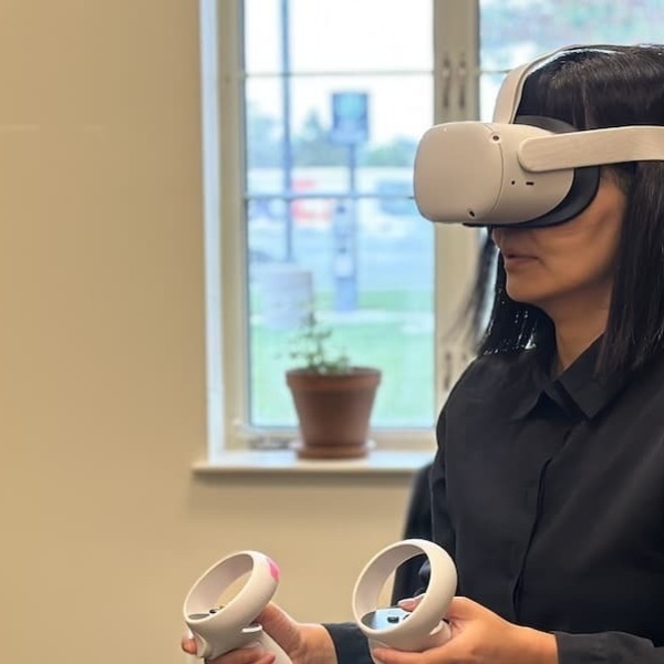 A university professor goes through a virtual reality experience while wearing a headset and holding a controller in each hand.