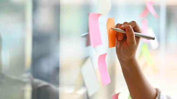 a photo of a hand writing on sticky notes attached to glass