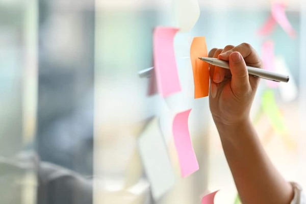 a photo of a hand writing on sticky notes attached to glass