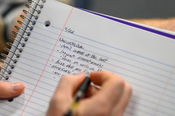Close-up of a hand writing notes in a spiral-bound notebook. The notes, dated 9/26, have a header of "New Criticism."