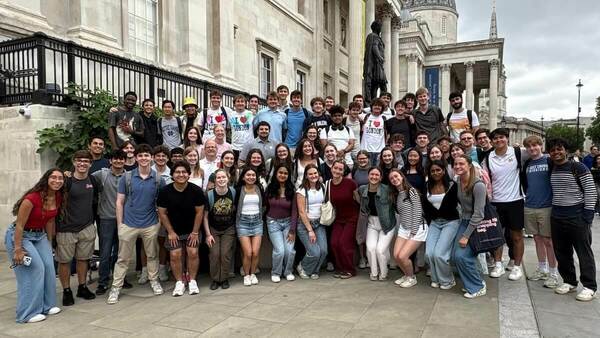A large group of people pose for a photo in front of a building in London's Trafalgar Square