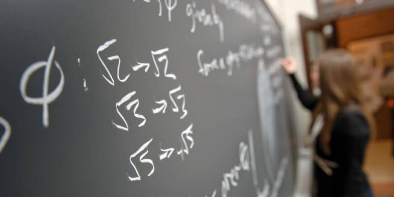 someone writing mathematical notations on a chalkboard