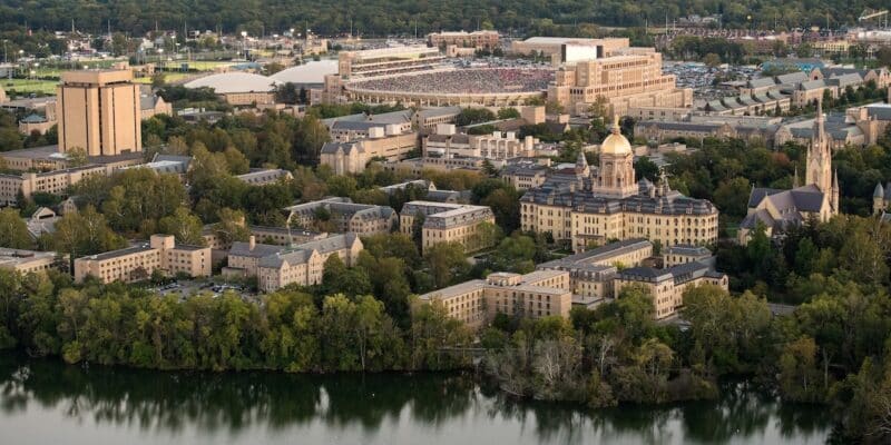 an aerial view of the Notre Dame campus looking to the southeast over Saint Mary's Lake, with the Golden Dome and other buildings in the foreground and Notre Dame Stadium in the distance in the background